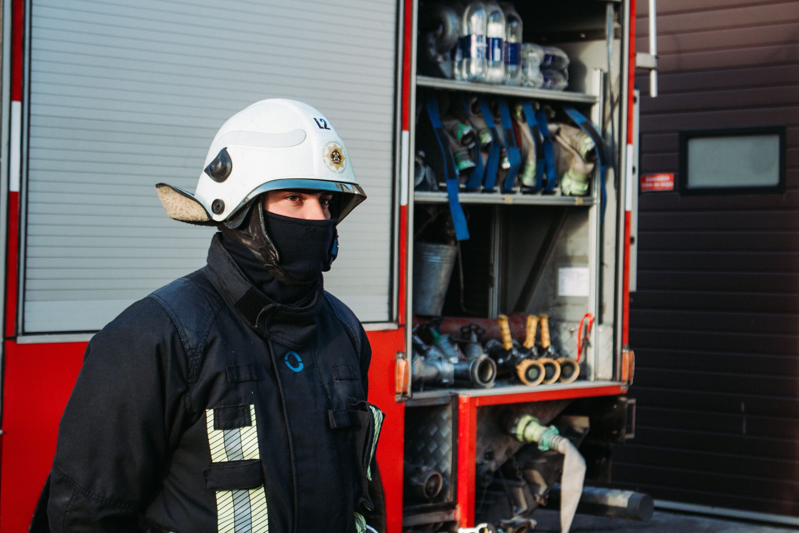 A firefighter in uniform stands beside a fire truck with equipment.